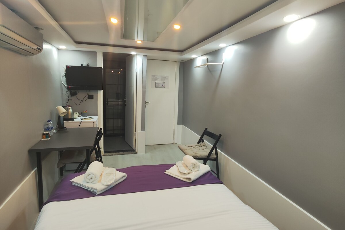 A compact hotel room with a bed, a desk, a chair, and a television.