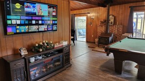 Ett mysigt rum med ett biljardbord, en öppen spis och en tv som visar olika streamingtjänster.