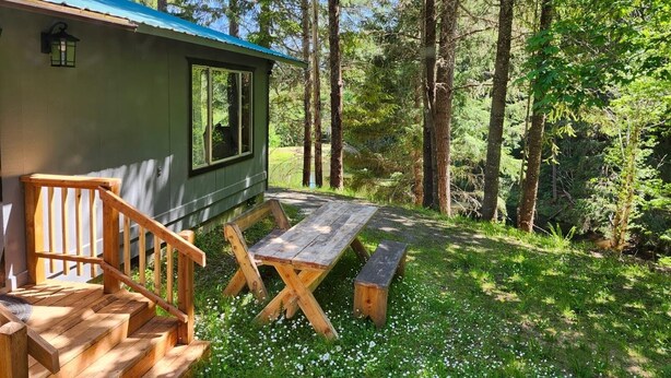En stuga med en träveranda, ett picknickbord och en bänk.