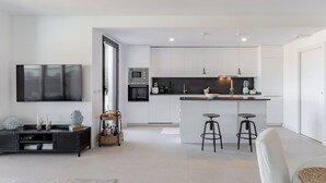 Eine moderne Küche mit weißen Schränken, einer zentralen Kochinsel mit Sitzgelegenheiten und einem an der Wand befestigten Flachbildfernseher.
