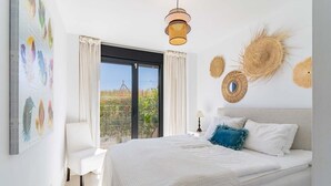 Ein Schlafzimmer mit einem großen Bett, einem Sessel, einem Fenster mit Vorhängen und Wandbildern.