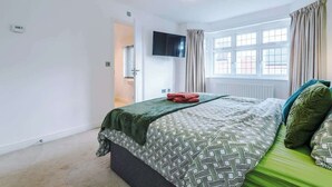 Une chambre à coucher avec un lit, une télévision, une fenêtre avec des rideaux et un radiateur.