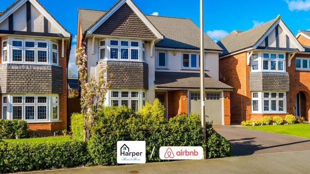Une rangée de maisons à deux étages, chacune dotée d’un garage, d’une allée et d’enseignes indiquant « Harper » et « Airbnb ».