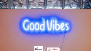 Une enseigne au néon avec l’inscription « Good Vibes » sur un mur, ainsi que les logos de Harper Home & Home et d’Airbnb.