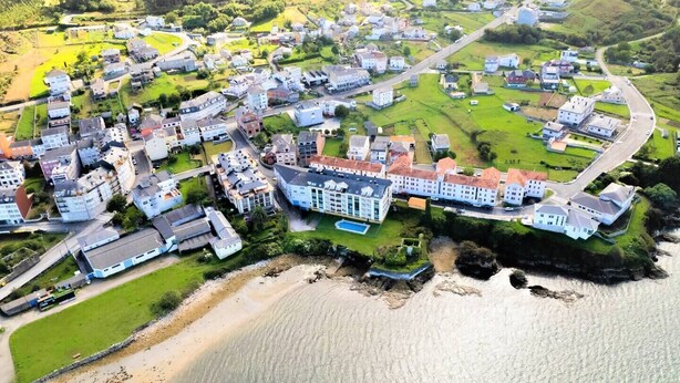 Vue aérienne d’une zone résidentielle côtière, avec des maisons, une plage et un pont.