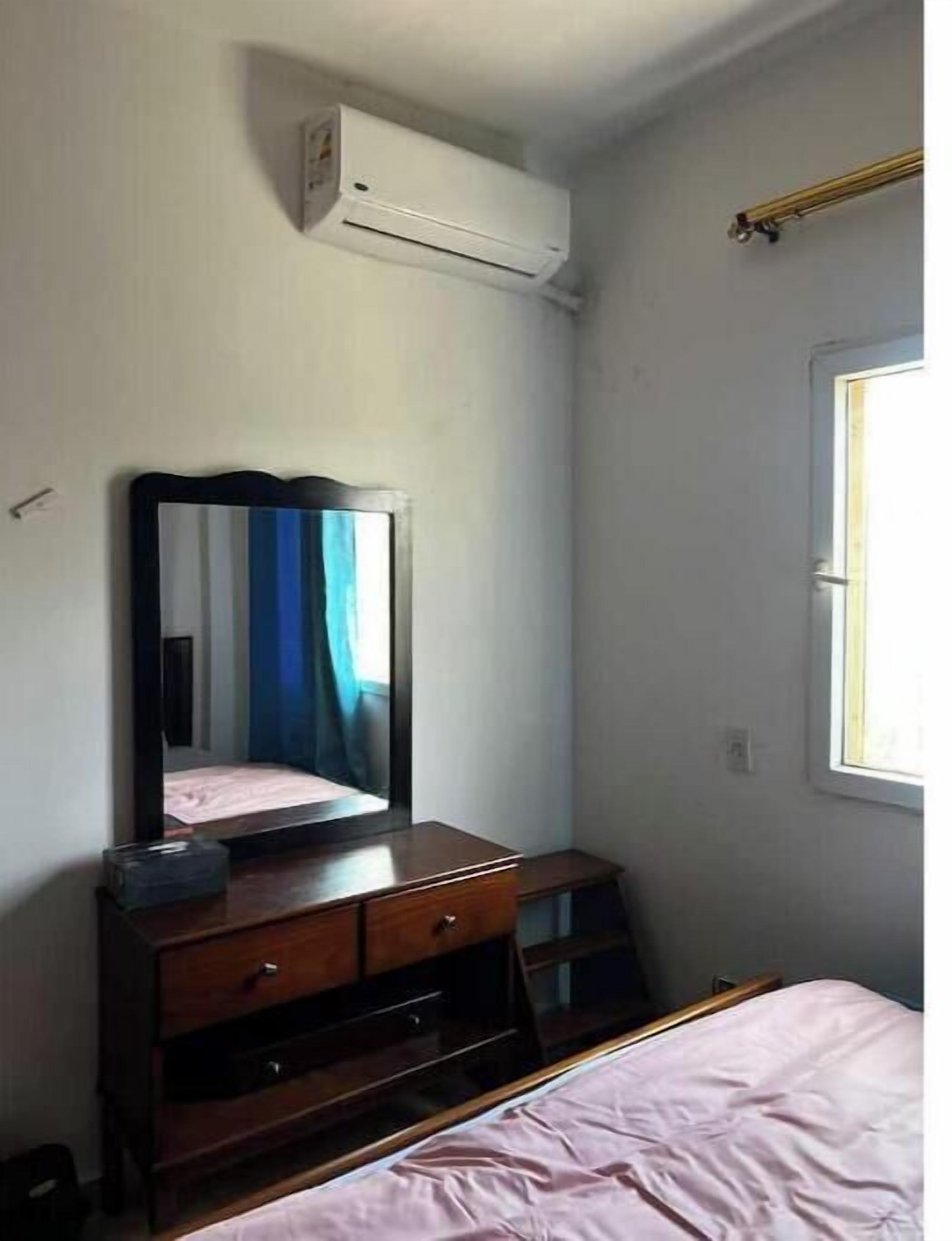 Un dormitorio con cama, cómoda, espejo y equipo de aire acondicionado en la pared.