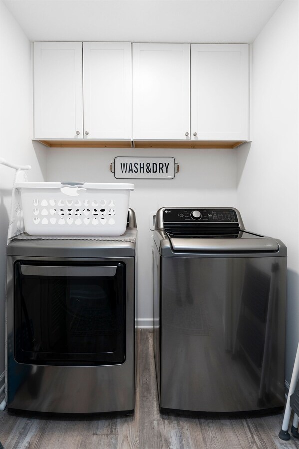 A laundry area with a washing machine and dryer, a white cabinet above, and a 'WASH&DRY' sign.