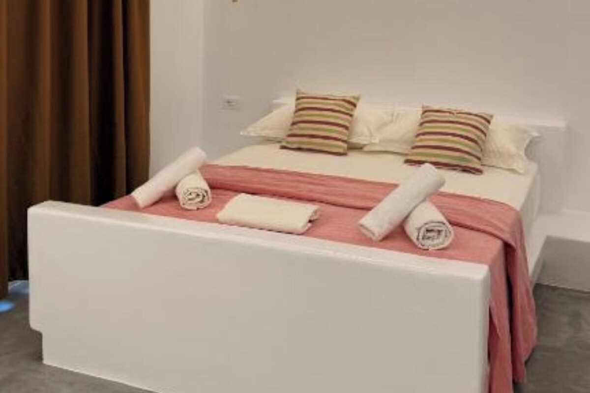 A modern bedroom with a white bed, pink bedding, and a brown curtain.
