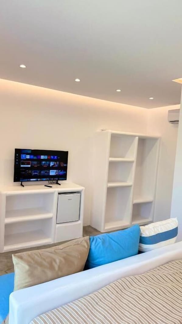 Ein modernes Wohnzimmer mit Fernseher, weißen Regalelementen und einem Sofa mit blauen und beigen Kissen.