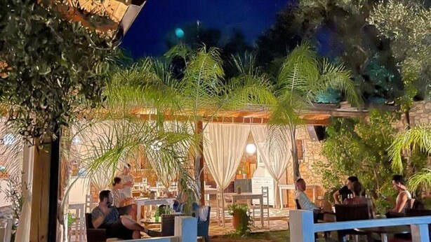 An outdoor seating area with tables and chairs, surrounded by greenery and a stone wall. - Rida Village Ksamil Island (Ksamil)
