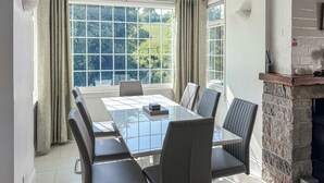 Een moderne eethoek met een glazen tafel, zes stoelen en een haard van baksteen.
