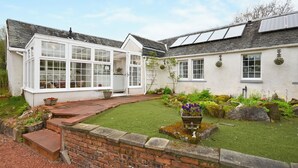 Een twee verdiepingen tellend huis met een conservatorium, een tuin met een vijver en zonnepanelen op het dak.