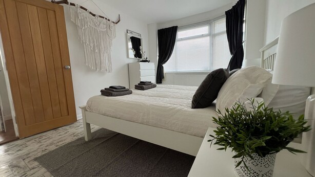 A bedroom with a bed, a bedside table with a plant, a wardrobe, a mirror, and a window with curtains. - modern Bungalow with hot tub, garden, bbq & Netflix 10 min drive to city centre (Southampton)