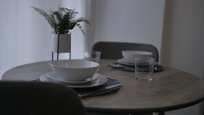 A round dining table with a white bowl, plates, and glasses. There is a potted plant on the table. - modern Bungalow with hot tub, garden, bbq & Netflix 10 min drive to city centre (Southampton)