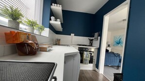A modern kitchen with white countertops, blue walls, and a small dining area with a table and chairs. - modern Bungalow with hot tub, garden, bbq & Netflix 10 min drive to city centre (Southampton)
