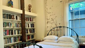 A bedroom with a metal bed frame, white bedding, and a bookshelf filled with books. - Spacious, artist-designed apartment in 1890s chocolate factory. DOG FRIENDLY! (Hopewell)