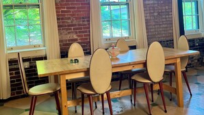 A dining area with a brick wall, large windows, and a wooden table with chairs. - Spacious, artist-designed apartment in 1890s chocolate factory. DOG FRIENDLY! (Hopewell)