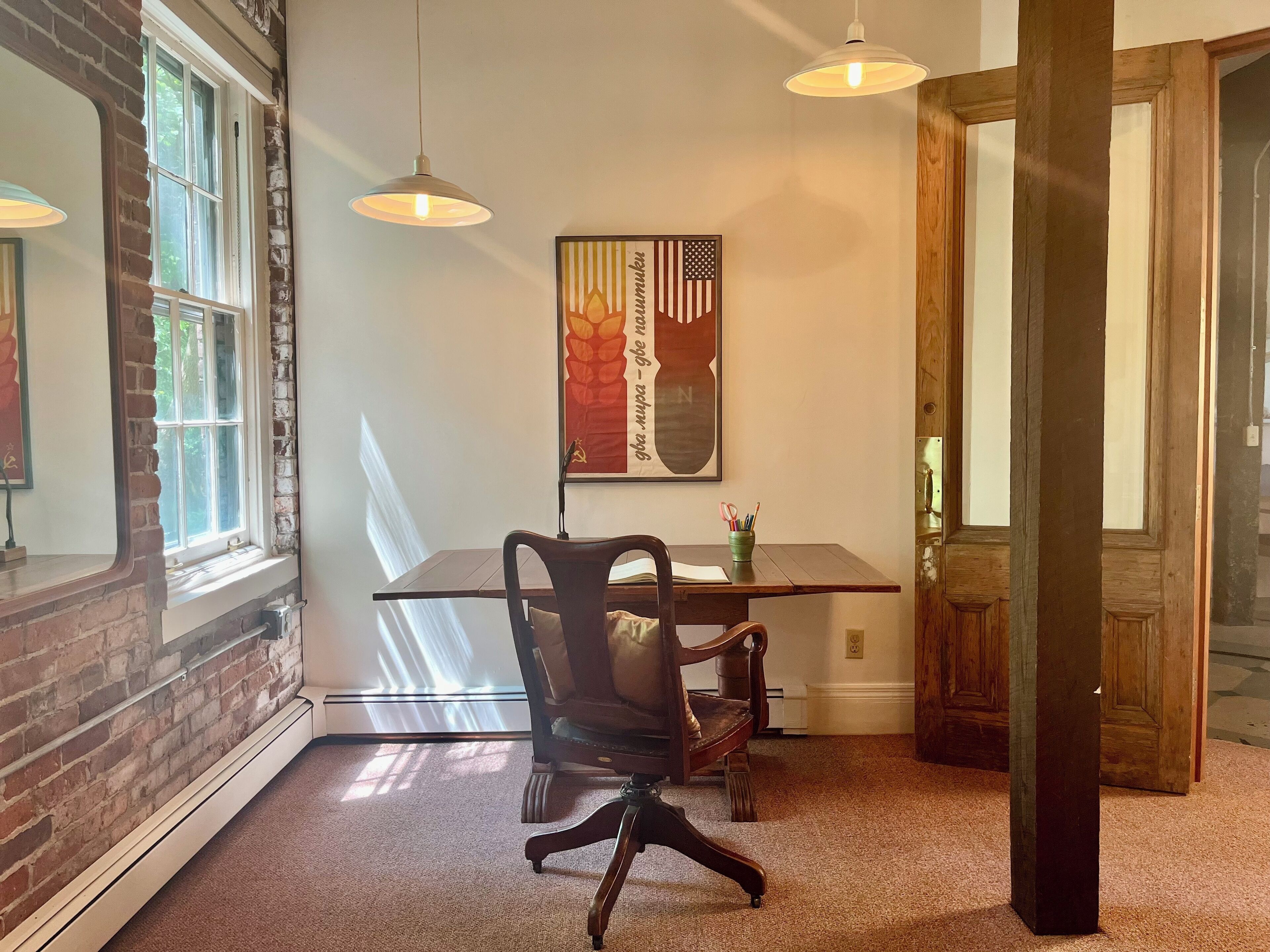 A dining area with a table, chairs, pendant lights, and a framed artwork on the wall.