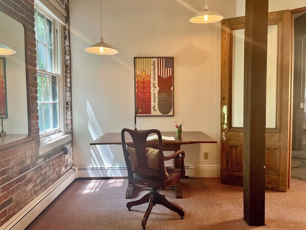 A dining area with a table, chairs, pendant lights, and a framed artwork on the wall.