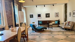 A dining area with a wooden table and chairs, a blue lounge chair, a sofa with teal cushions, and a patterned floor. - Spacious, artist-designed apartment in 1890s chocolate factory. DOG FRIENDLY! (Hopewell)
