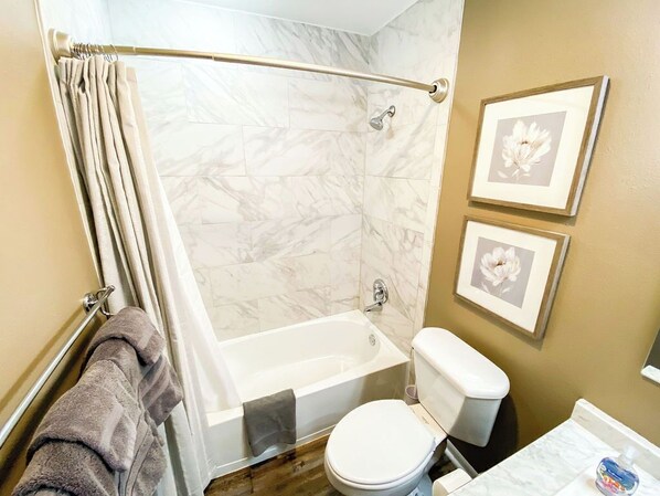 A bathroom with a bathtub, toilet, and shower curtain. There are framed pictures on the wall.