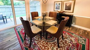 Un coin repas avec une table en verre entourée de chaises en osier, un tapis à motifs et un lustre.