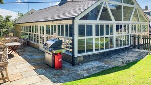 A conservatory with a tiled roof, large windows, and a barbecue grill.
