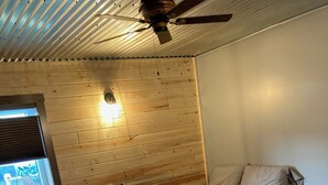 A room with two beds, a window with blinds, a ceiling fan, and a wooden wall. - Newly built in Devils Lake, Perfect for Fishing or Relaxing (Devils Lake)
