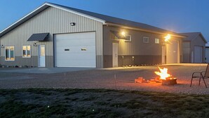 A large industrial building with a garage door, a fire pit with logs, and a chair. - Newly built in Devils Lake, Perfect for Fishing or Relaxing (Devils Lake)