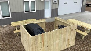 A building with a garage, a covered outdoor seating area with benches, and a sign for 'RK's Lodging'. - Newly built in Devils Lake, Perfect for Fishing or Relaxing (Devils Lake)