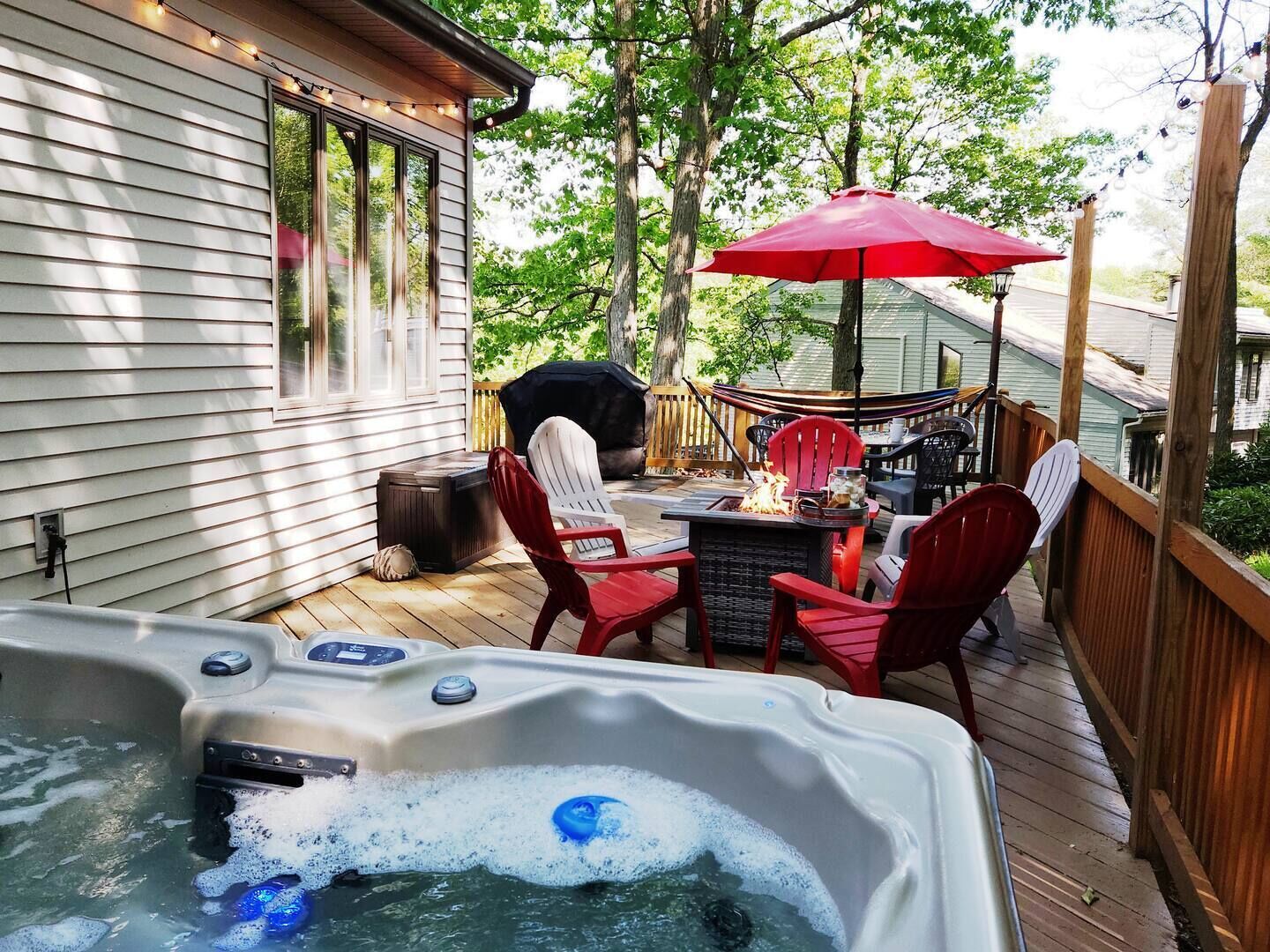 A hot tub on a wooden deck with outdoor furniture and a barbecue grill.