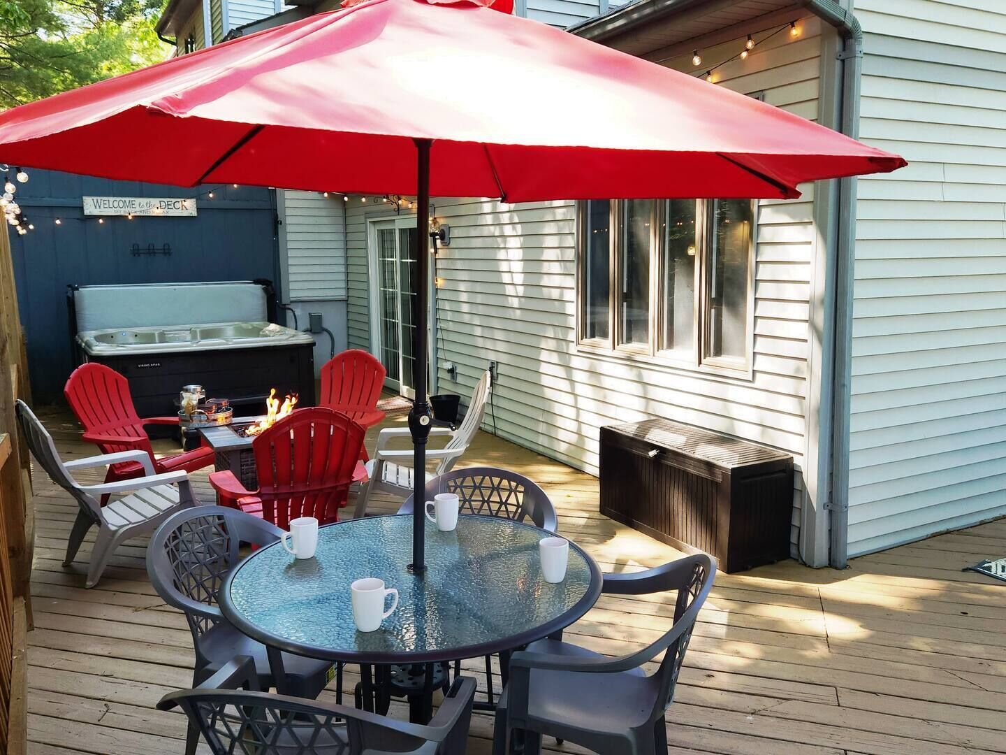 Une terrasse avec une table et des chaises en verre, un parasol rouge et un jacuzzi.
