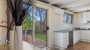 A modern kitchen with white cabinets, a stainless steel dishwasher, and a window overlooking a garden.