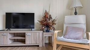 A modern living room with a flat-screen TV on a wooden TV stand, a decorative plant, and a white armchair with a cushion.