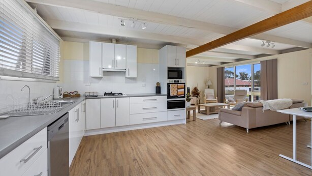 A modern kitchen with white cabinets, a built-in oven, and a dining area with a sofa and table.
