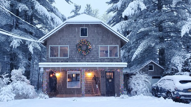 A two-story house with a front porch, a visible door, and a wreath on the wall.