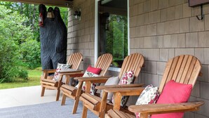 A covered porch with wooden Adirondack chairs, a stone statue, and a view of the greenery.