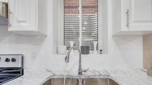 A kitchen with a double sink, white cabinets, and a window with a view of a brick wall. - Hidden Gem: Spacious Basement (Milton)