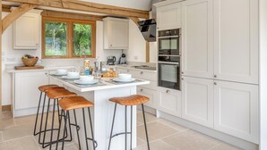 Una cocina moderna con armarios blancos, una isla central con taburetes y electrodomésticos integrados.