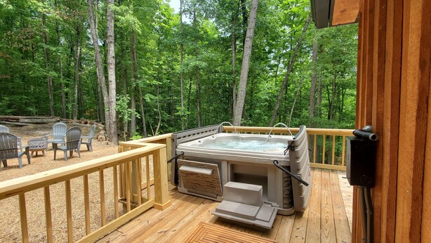 A wooden deck with a hot tub, outdoor seating, and a view of a forest. - Nestled in the Woods (Campton)