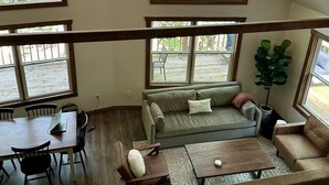A spacious loft with high ceilings, large windows, a dining area, and a cozy seating area with a sofa and coffee table. - Nestled in the Woods (Campton)