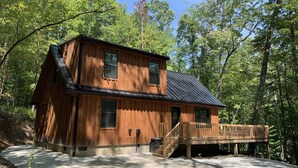 A two-story wooden cabin with a deck, surrounded by trees. - Nestled in the Woods (Campton)