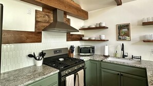 A kitchen with green cabinets, a stainless steel stove, a microwave, and a wooden staircase. - Nestled in the Woods (Campton)