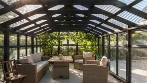Une serre aménagée avec des meubles en osier, une table et un banc.