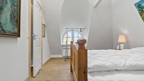 Une chambre à coucher avec un lit en bois, du linge de lit blanc, une lampe de chevet et un tableau au mur.