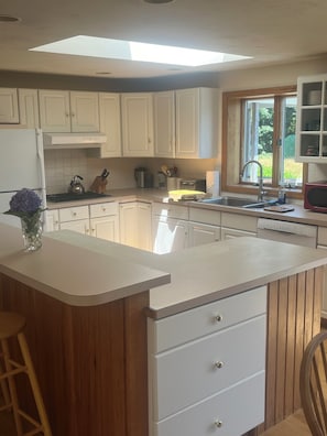 Cozinha moderna com armários brancos, uma ilha central, claraboia e vista para o verde lá fora.