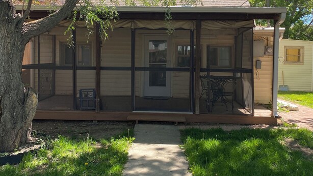 A covered porch with a sliding glass door, a small outdoor seating area, and a pathway leading to the door.