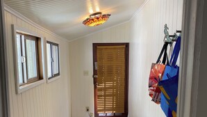 A hallway with white paneled walls, a patterned carpet, a ceiling light fixture, and a door with blinds.