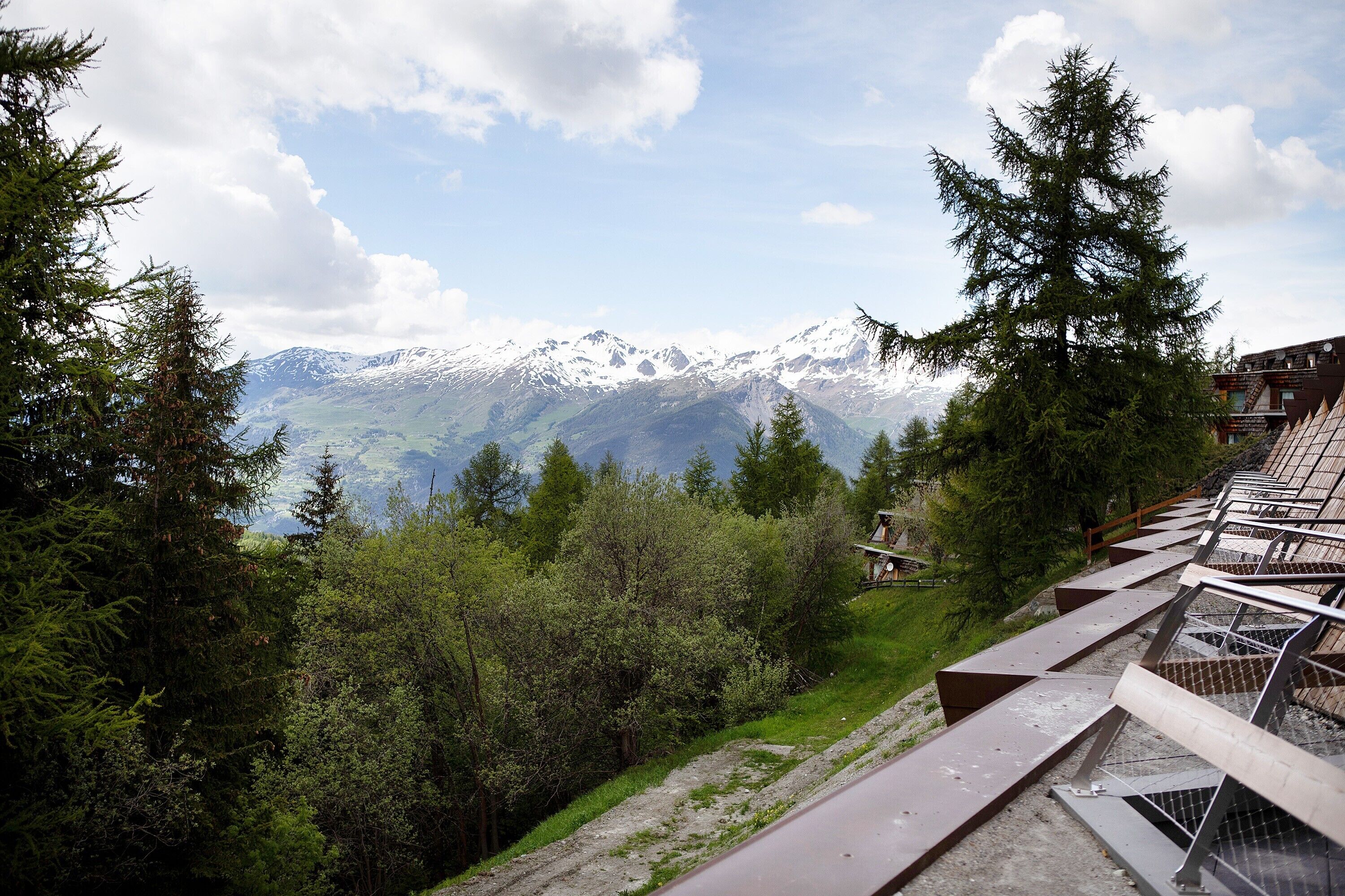 A mountain view with snow-capped peaks, a forested area, and a building with a sloped roof.