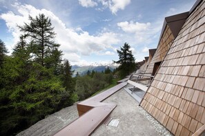 A pathway leading to a building with a view of snow-capped mountains and dense forest.